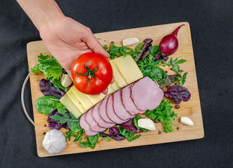 Female hands put tomato on board with cheese, ham, lettuce, garlic, onion. Food decoration concept.