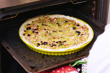 Homemade tart with leek bacon and dried plum placed into hot oven. Savory quiche preparation step...