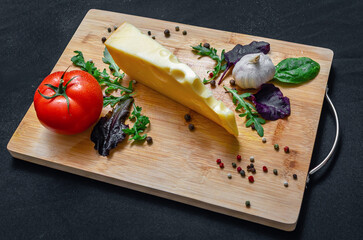 Cheese with mixed salad, tomatoes, garlic and pepper on wooden board on black. Healthy food.