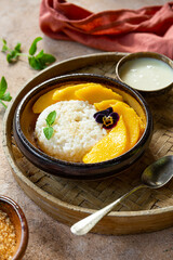 Thai mango sticky rice with coconut milk, garnished with edible flowers on light background
