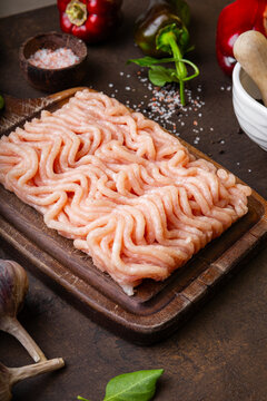 Raw chicken minced meat on cutting board and ingredients. Ground meat with ingredients for cooking on dark background vertical photo