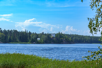 White stone castle tower on forested hill above lake in summer