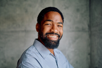 Black man with a beard smiling against a grey background, expressing happiness, friendliness, and...