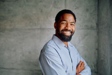 Black businessman looking at camera, smiling broadly with folded arms, expressing confidence in a professional setting