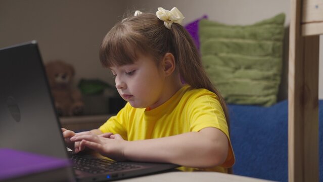 a child girl does her homework on a laptop, online distance learning on computer, schoolgirl does her homework, little kid wants to get a school education, play game on Internet, chat with classmates.
