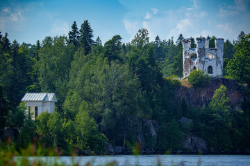 White stone castle tower on forested hill above lake in summer
