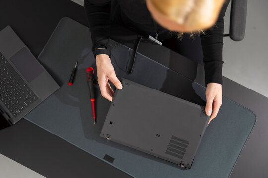 Female IT technician in her 30s repairs laptop at a dark desk with tools nearby