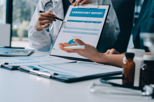 Medical team meeting analyzing blood test results in hospital laboratory. Doctors and scientists in lab coats are having a discussion about blood test result, holding test tubes and taking notes.