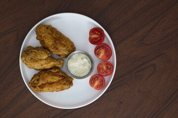 Fried chicken wings with garlic sauce and cherry tomatoes on a white plate.