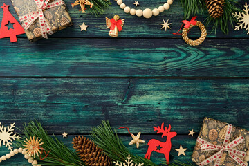 Rustic Christmas flat lay with pinecone gifts, straw ornaments, red cutouts, and pine branches on teal wood table. Top view.