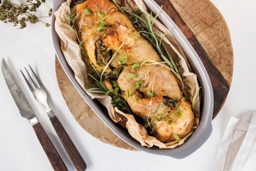 Delicious roast chicken, stuffed with herbs and spices, is presented in a baking dish lined with parchment paper. It is ready to be served at a dinner party