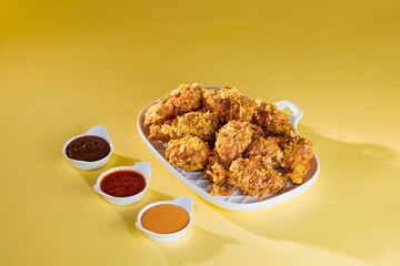 Crispy, golden fried chicken pieces are piled high on a fancy white platter, next to little bowls filled with sauces including barbecue, chili, and a creamy dip, all on yellow