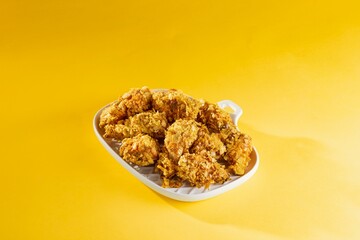 A pile of golden fried chicken pieces sits on a white plate, ready to be enjoyed. The vibrant yellow background emphasizes the tempting, crispy texture