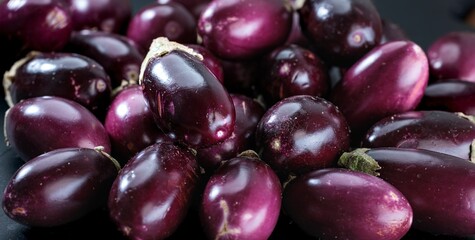 A collection of deep purple eggplants are arranged close together. Their smooth, shiny surfaces catch the light, creating a vibrant and appealing display of fresh produce