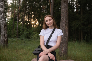 Obraz premium Young woman with long hair wearing a white shirt and black skirt stands confidently in a lush green forest, showcasing a serene outdoor lifestyle and natural beauty