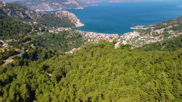 aerial perspective showcasing the picturesque Turunc Bay, nestled along the stunning Mediterranean coastline of Turkey. Lush green forests blanket the surrounding hills, leading down to the charming v