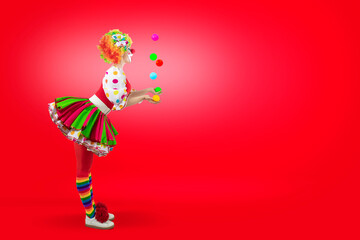 Surprised juggler female clown juggling balls in the circus, woman entertainer as Joker in suit and wig, with clown whiteface makeup. Trickster, jester, pantomime, mime,  professional actor at events