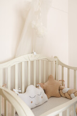  Cozy baby crib with soft pillows in cloud and star shapes, beige braided bumper and delicate canopy. Minimalist nursery interior design, safe sleeping place for newborn or infant in pastel colors. 