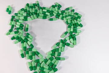 Green capsules arranged in a heart shape on a clean, white background symbolize healthcare, medicine, or a love of pharmacy.