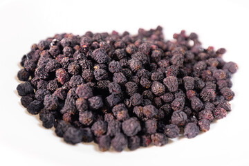 Detailed macro view of a dense, wrinkled, dark, dried  berries pile showing texture and natural variations. White background.
