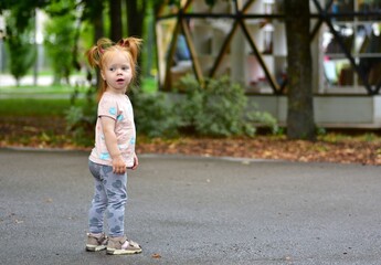 Red-haired toddler girl with pigtails standing on wet asphalt in park. Child enjoying outdoor exploration, carefree play, and happy childhood moments after rain.
