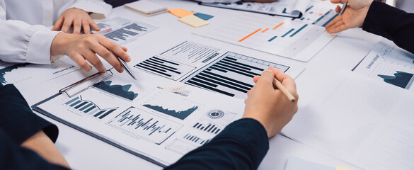 A collaborative business meeting scene depicting several hands engaged in analyzing financial reports and charts while discussing strategies and insights around a conference table. SACTR