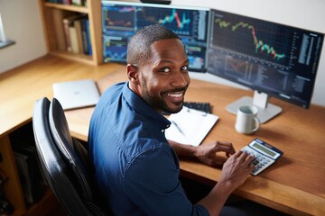 Smiling man looks at camera while working on financial data at his home office