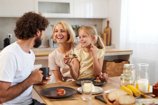 Family members gather around the kitchen table, sharing joyful moments and breakfast. The atmosphere is warm and inviting, filled with laughter and tasty meals.