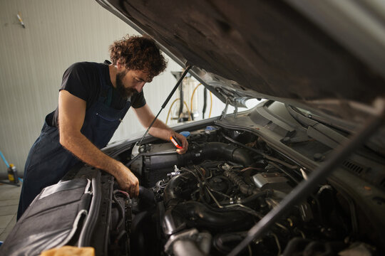 A skilled mechanic works on a car's engine, using tools to check and repair parts. The setting is a well-equipped garage with various tools and equipment around.
