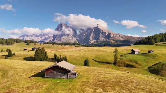 Aerial view over meadows in front of Alpe di Siusi peaks, in Dolomites, Italy. Beautiful hut on alpine plateau Seiser Alm. Wooden cabins in south Tyrol. Dolomites UNESCO World Heritage.