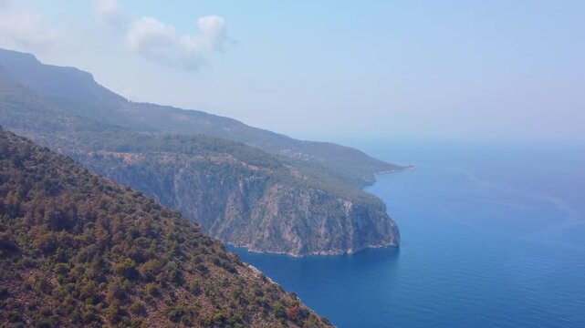 aerial drone shot captures the stunning natural beauty of Oludeniz, Turkey. Lush green mountains meet the vibrant turquoise waters of the Mediterranean Sea, showcasing the rugged cliffs and serene coa
