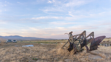 A winding dirt path leads through a grassy field with trees under a bright blue sky with wispy clouds