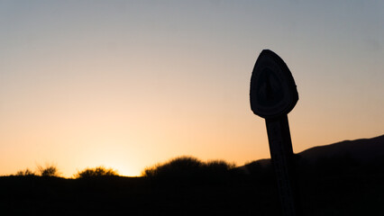 Silhouette of person standing on a hill against a bright sunset with mountains in the background © Rodrigo