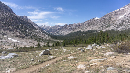 Mountain valley vista with a hiking trail winding through rocky terrain under a clear blue sky above