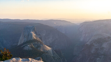 Aerial view of half dome mountain with hazy sky and layered mountain ranges in the background at sunset