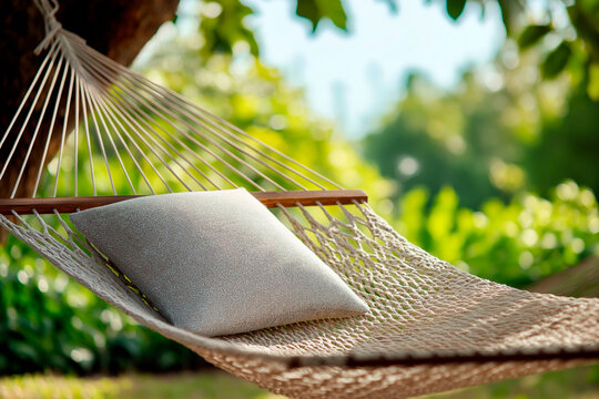 Cozy beige pillow resting on a woven rope hammock suspended between trees in a lush green garden on a sunny day