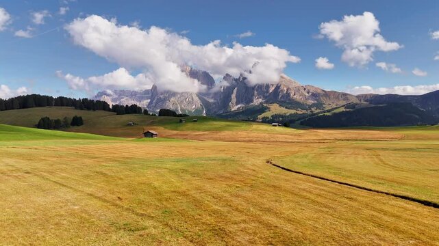Aerial view over meadows in front of Alpe di Siusi peaks, in Dolomites, Italy. Beautiful hut on alpine plateau Seiser Alm. Wooden cabins in south Tyrol. Dolomites UNESCO World Heritage.