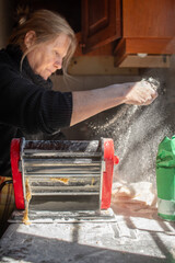 Mujer mayor caucásica hermosa y natural amasando tallarines caseros echando harina 