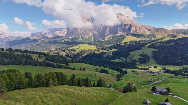 Aerial view over meadows in front of Alpe di Siusi peaks, in Dolomites, Italy. Beautiful hut on alpine plateau Seiser Alm. Wooden cabins in south Tyrol. Dolomites UNESCO World Heritage.