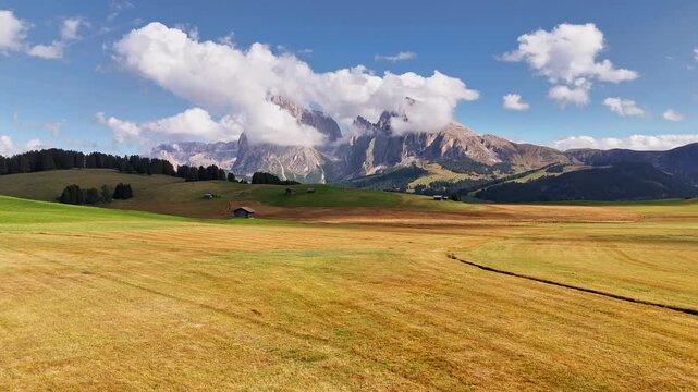 Aerial view over meadows in front of Alpe di Siusi peaks, in Dolomites, Italy. Beautiful hut on alpine plateau Seiser Alm. Wooden cabins in south Tyrol. Dolomites UNESCO World Heritage.