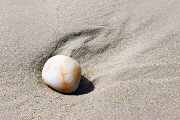 Ein Stein am Sandstrand mit Spuren im Sand, ausgelöst durch ablaufendes Wasser bei Ebbe
