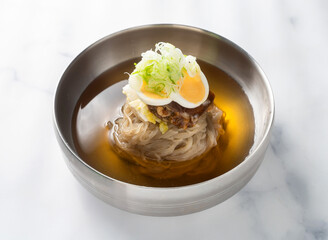 Korean Naengmyeon Cold Buckwheat Noodles with Broth, Boiled Egg, and Sliced Green Onion on marble background side view