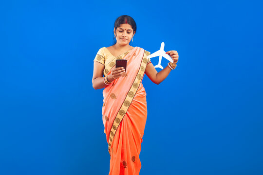 Indian female in sari presenting a paper airplane model and mobile phone representing tourism, travel planning, and digital connectivity.