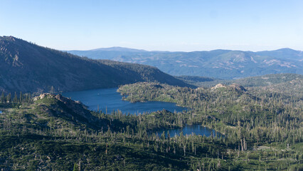 Aerial view of a serene lake surrounded by lush green forests and distant mountain ranges on a clear day