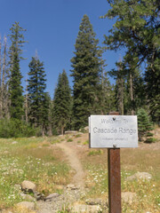 Welcome sign to cascade range with trees and a path in a meadow on a sunny day in the forest