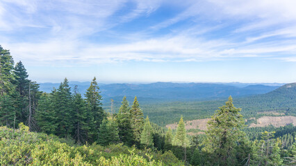 Overlook of forested mountains under a bright blue sky with wispy clouds in the distance view landscape