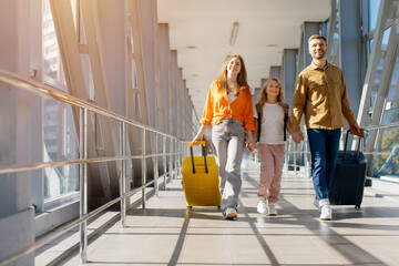 Caucasian family walking together at airport with luggage, holding hands and smiling in bright corridor, showing cheerful lifestyle, bonding and happy holiday travel © Anastasiya