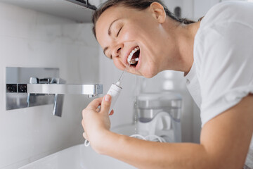A young woman uses a water flosser to clean her teeth in the bathroom in the morning. Concept:...
