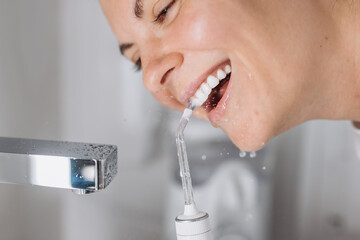 Close-up of a woman cleaning her teeth with a white portable water flosser. Concept: oral care and...