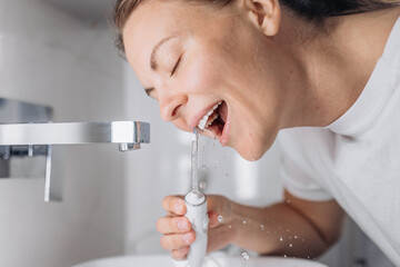 Close-up of a woman cleaning her teeth with a white portable water flosser. Concept: oral care and...